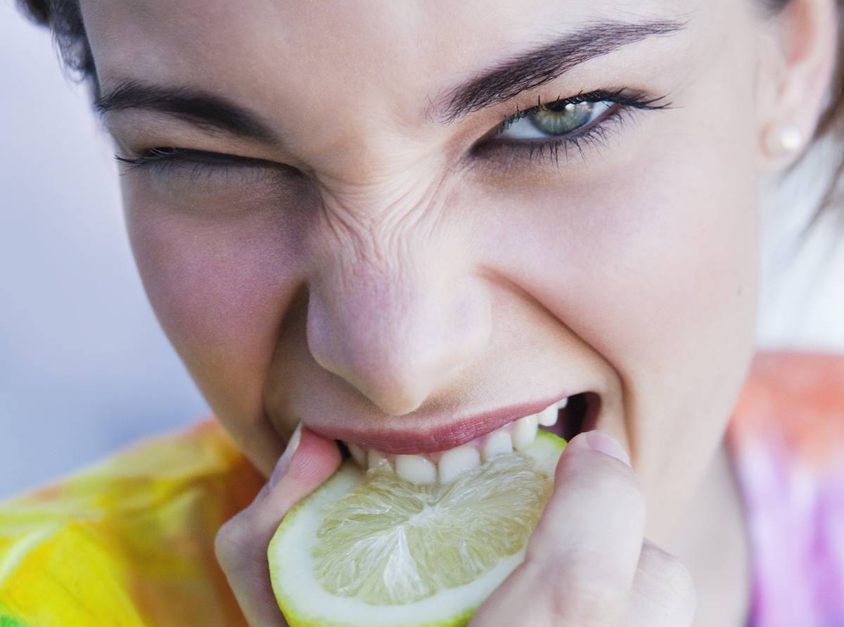 Боль во рту после еды. Человек ест лимон. Кислый. Кислый вкус.